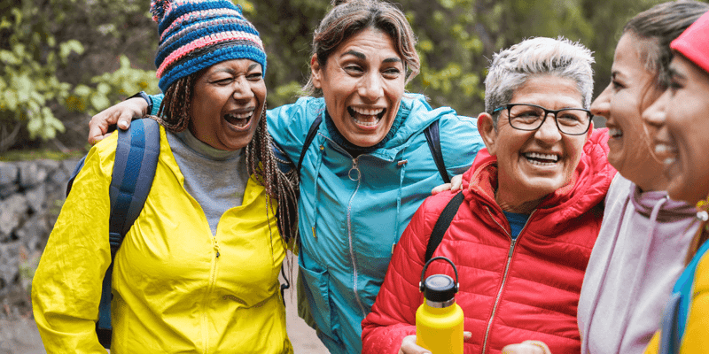 A group of five people laughing together outdoors in colorful jackets